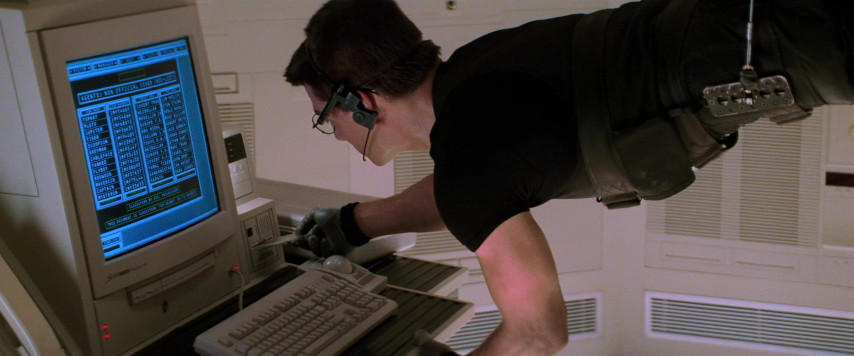 An image from the movie "Mission: Impossible". Ethan Hunt, hanging from cables, inserts a disk in a computer.