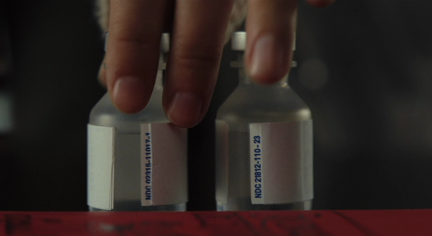 An image from the movie "Knives Out". Marta examines two vials of medicine.