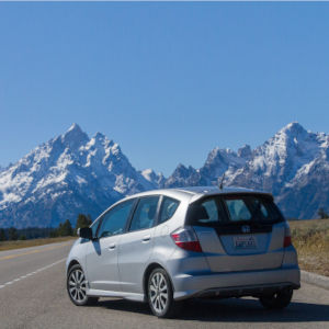 A silver hatchback is parked diagonally on a lonely road with two snow-capped mountains in the distance.