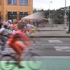 A photograph of a city street. a mass of colorful cylists fill the street on one side of the image, but fade away to reveal an empty street on the other side.